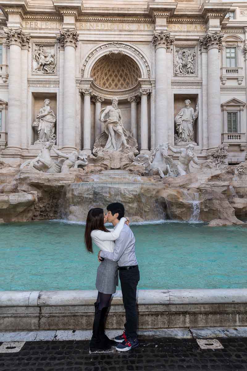 Couple kissing in front of the water fountain with the statues in the background