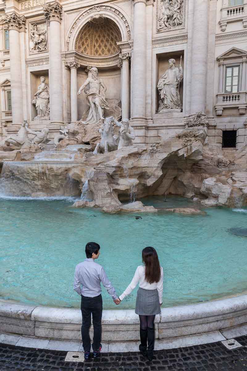Holding hands and looking and admiring together the beauty of Fontana di Trevi
