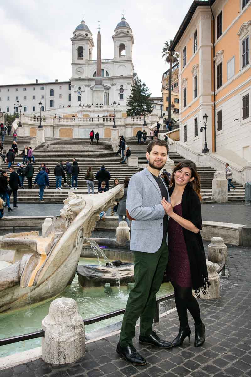 Couple portrait standing next to the barcaccia water fountain found at the bottom of the Spanish steps