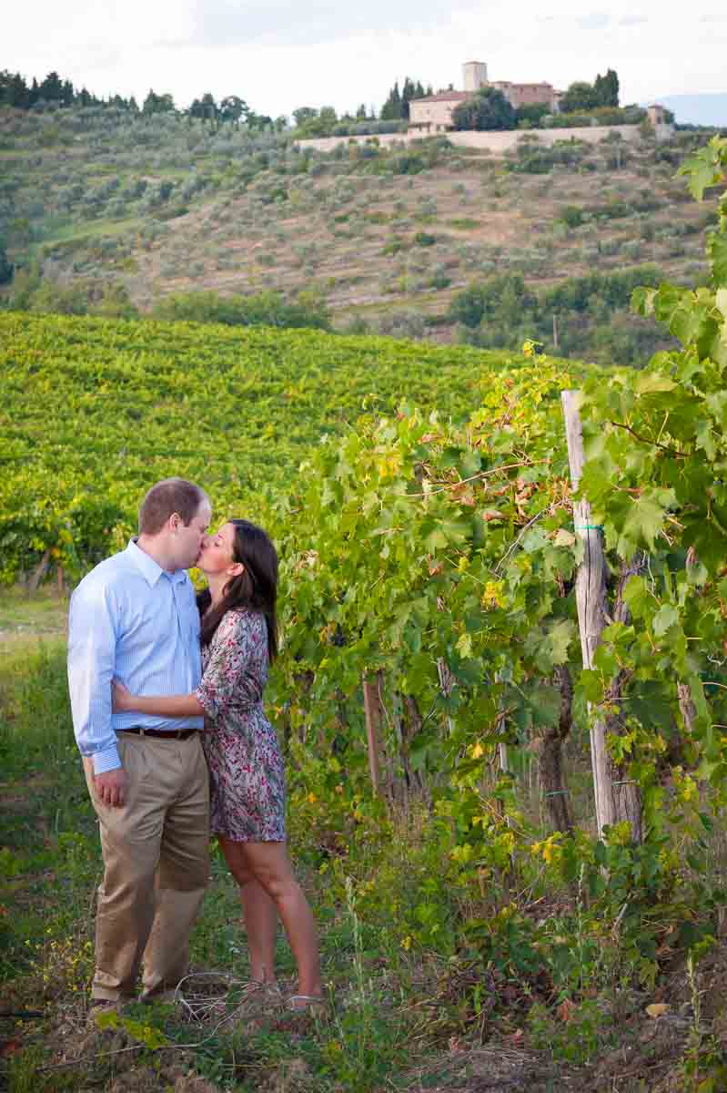 Couple kissing in a vineyard with the town Greve in Chianti Italy in the far distance during a Tuscany PhotoShoot