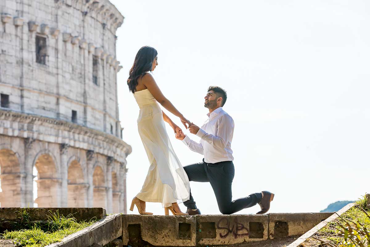 Chivalry moment of groom kneeling down before his wife to be in front of the Coliseum