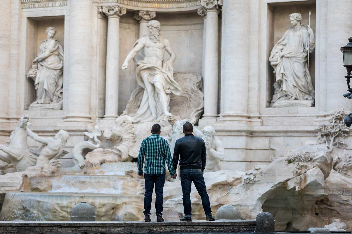 Couple holding hands and looking at the Trevi fountain marble statues from a distance