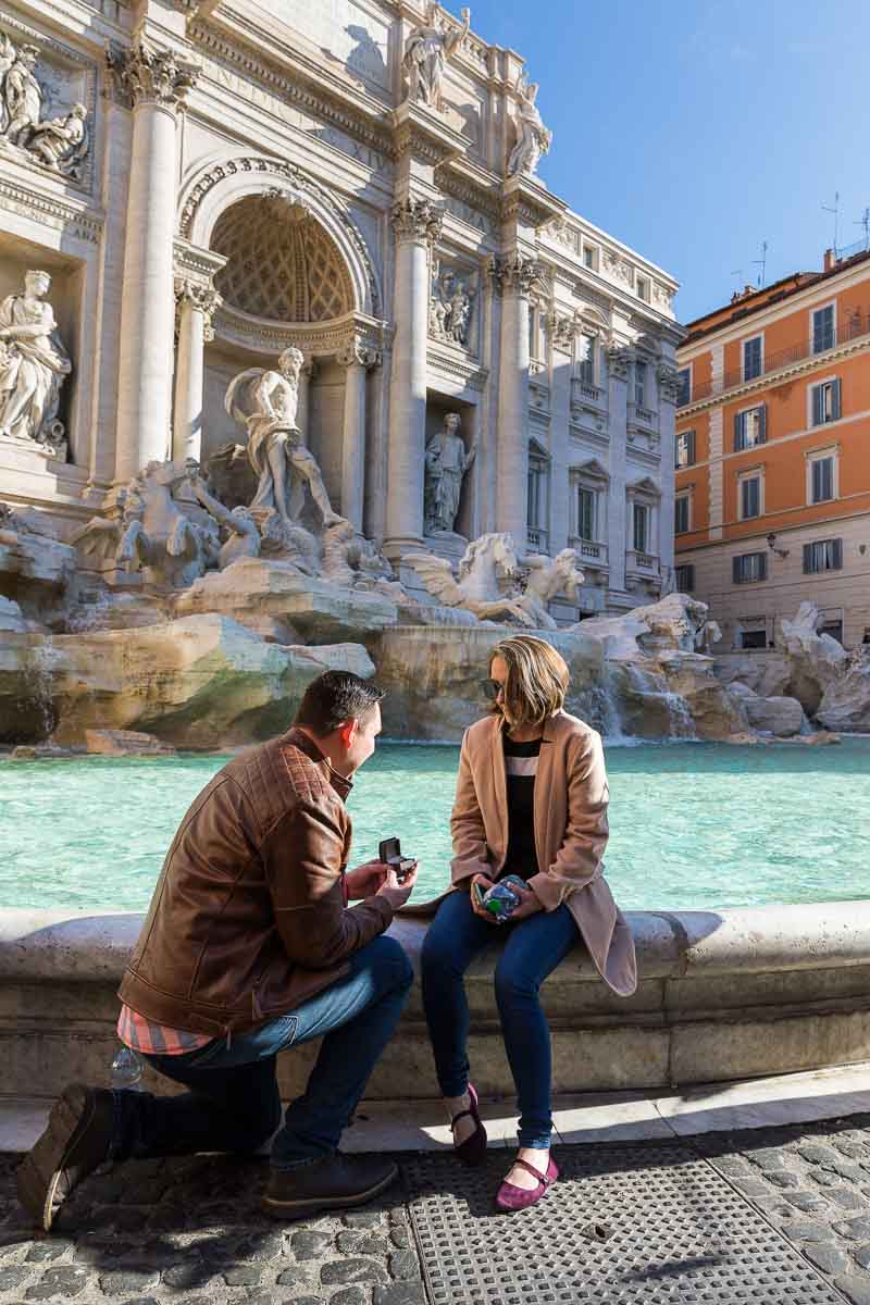 Man proposing knee down at the water edge of the Trevi fountain in the city of Rome Surprise Wedding Proposal