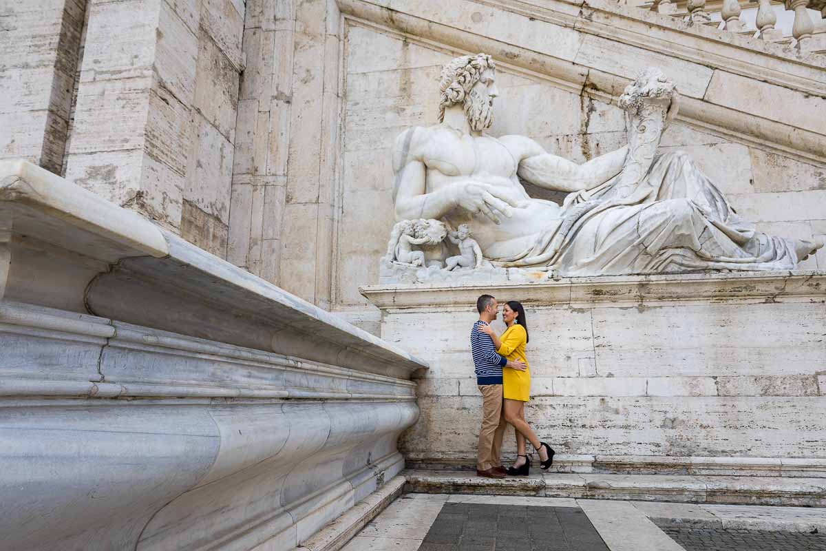 Posed photo of a couple underneath an ancient roman marble statue found in Piazza del Campidoglio