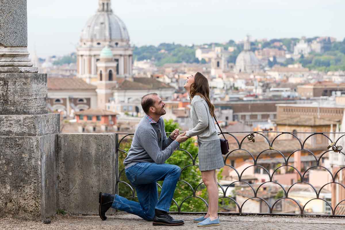 Man kneeling down during a surprise wedding proposal taking place at the scenic parco del pincio terrace in Rome Italy