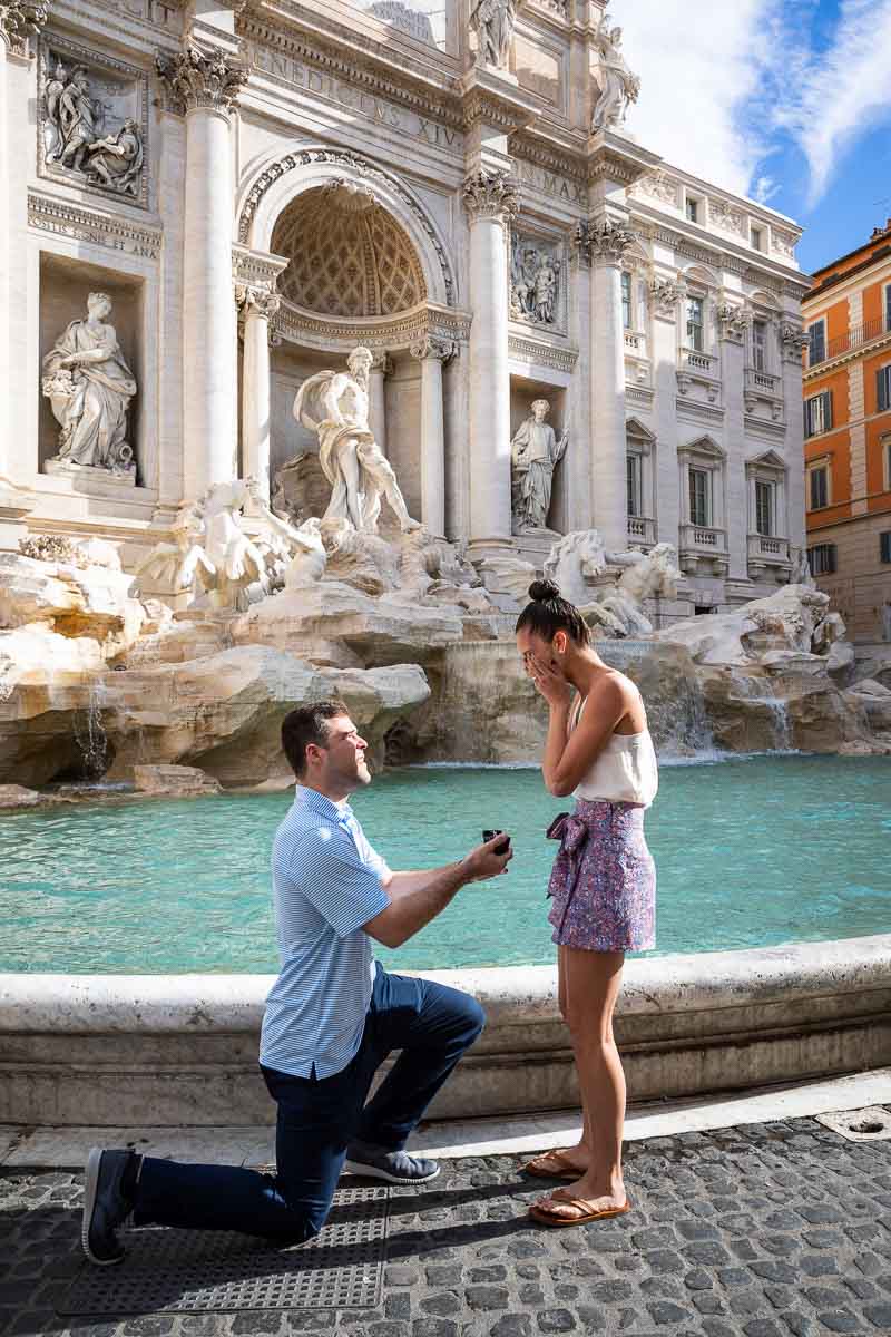 Man kneeling down with engagement ring in hand asking the big question in Rome's Trevi fountain
