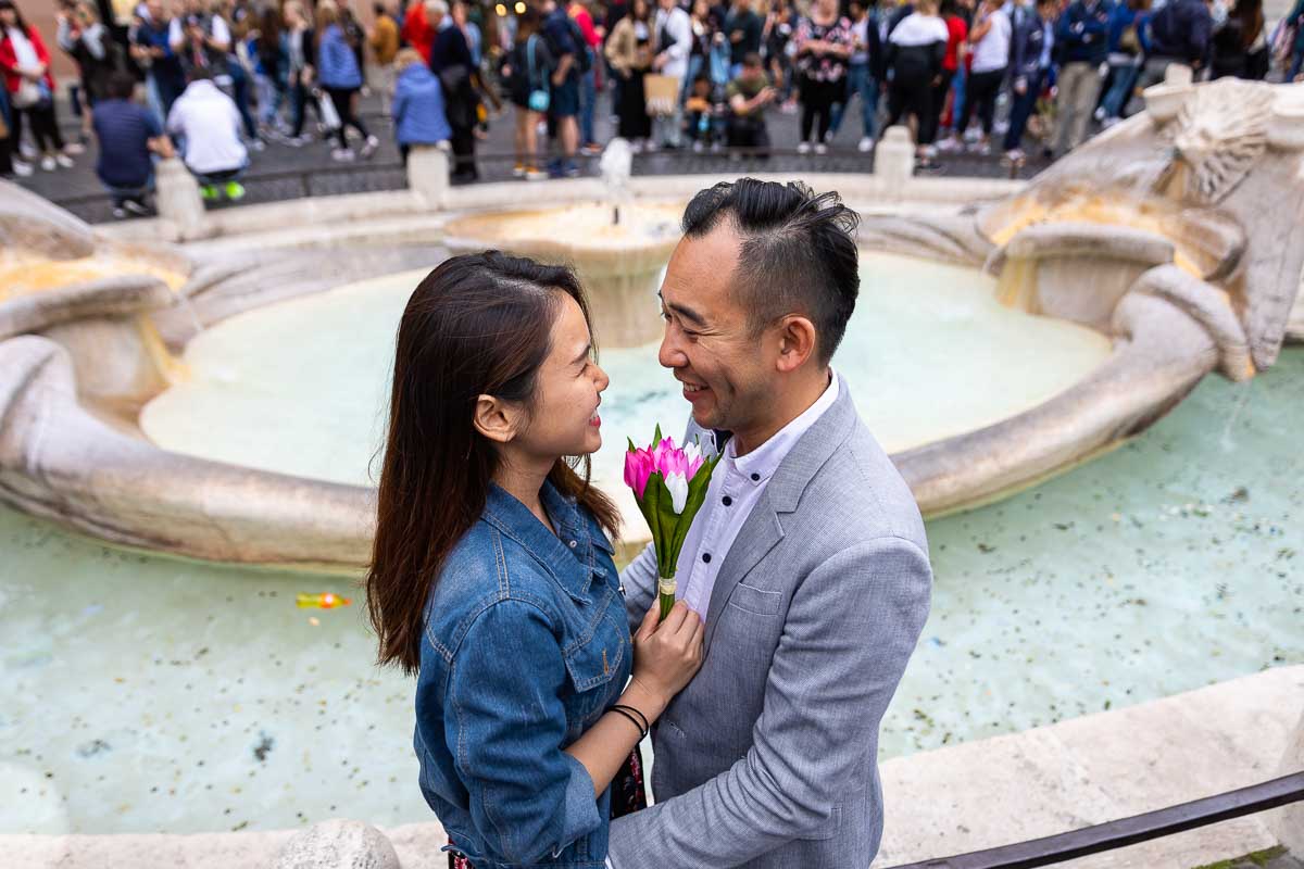 Engagement picture of a coupe close to one another before the Barcaccia water fountain found at the bottom of the Spanish steps