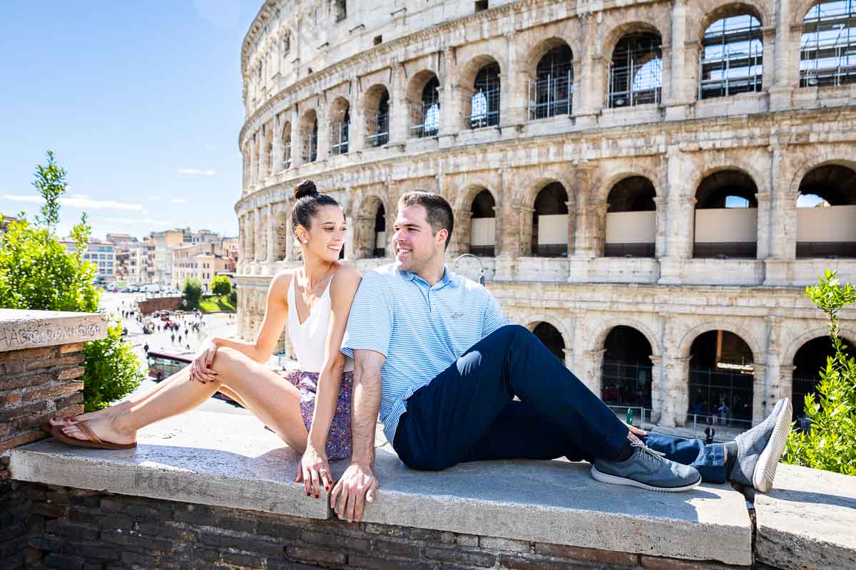 Sitting down portrait of a couple looking at each other with the coliseum in the background