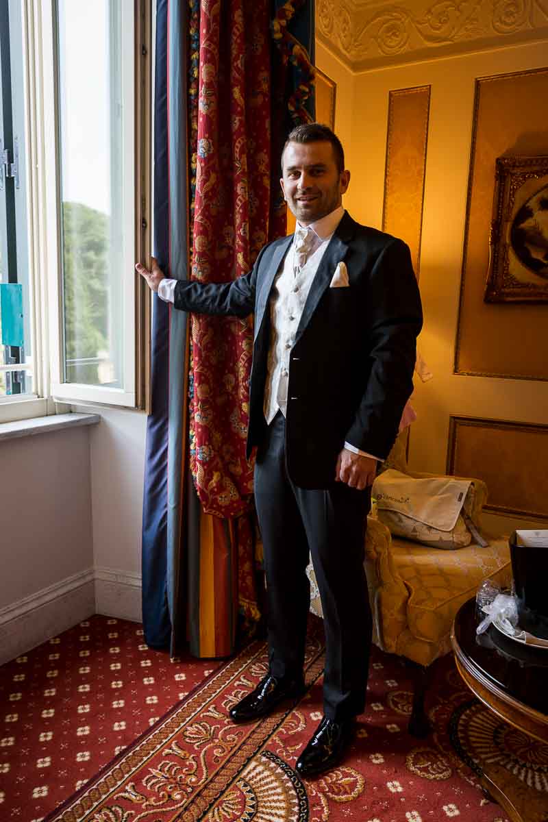 Groom portrait standing full view in front of the hotel room window