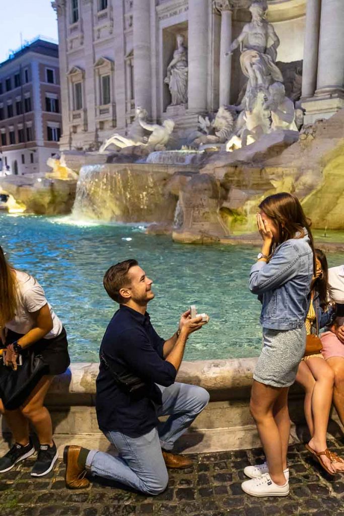 Man knee down nighttime surprise wedding proposal at the Trevi fountain