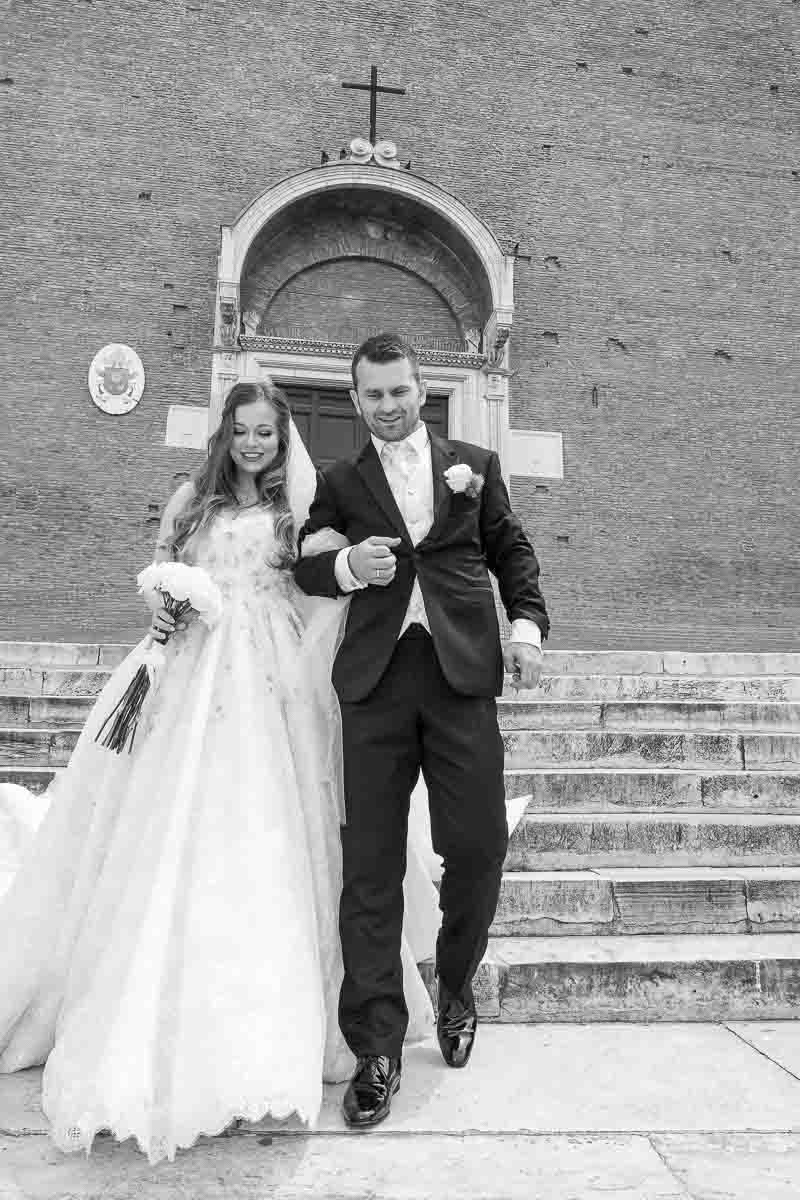 Newlyweds walking together out of the church and descending the steps of church Santa Maria in Aracoeli in black and white