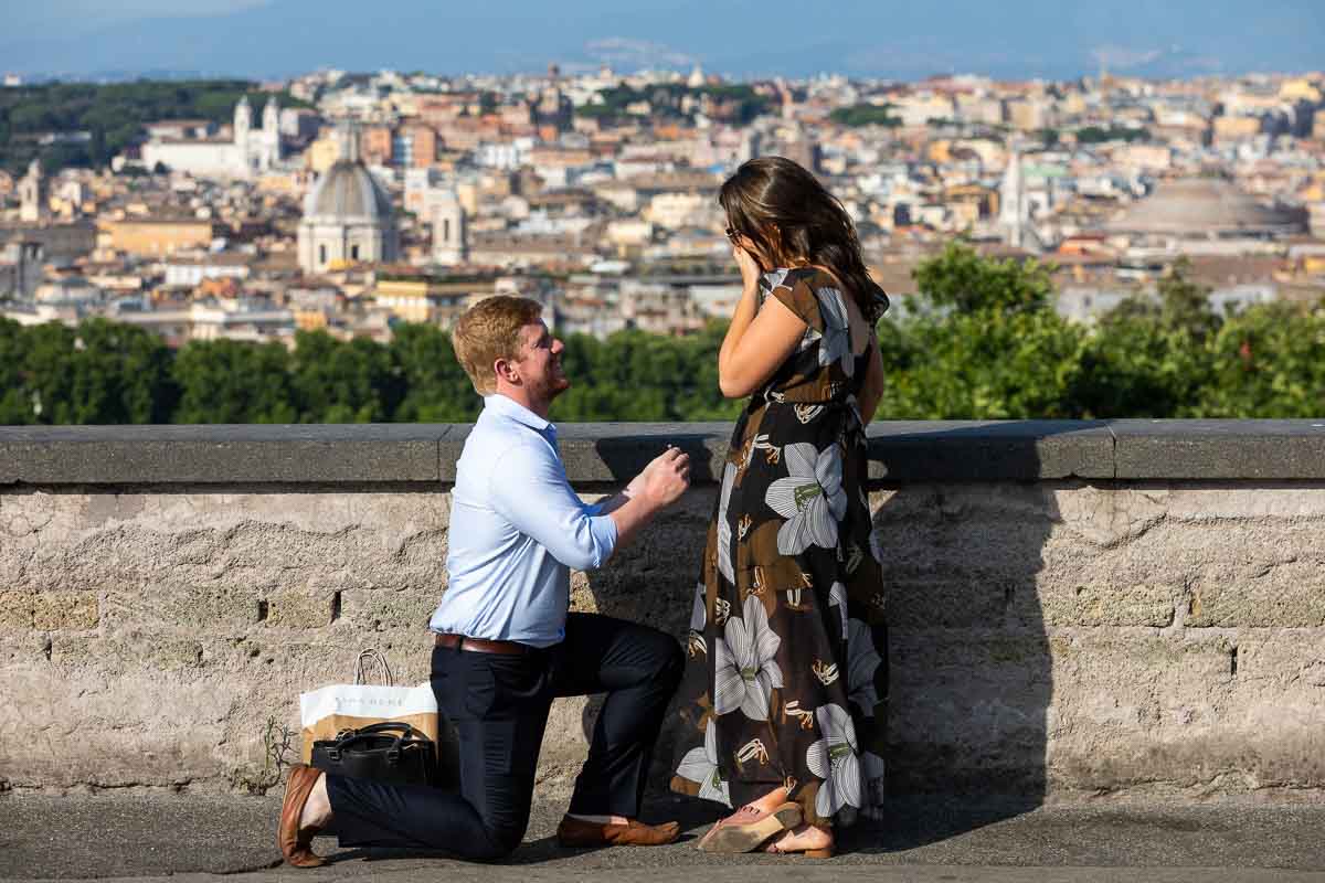 Man kneeling down proposing wedding overlooking the scenic view of the Rome panorama in the background.