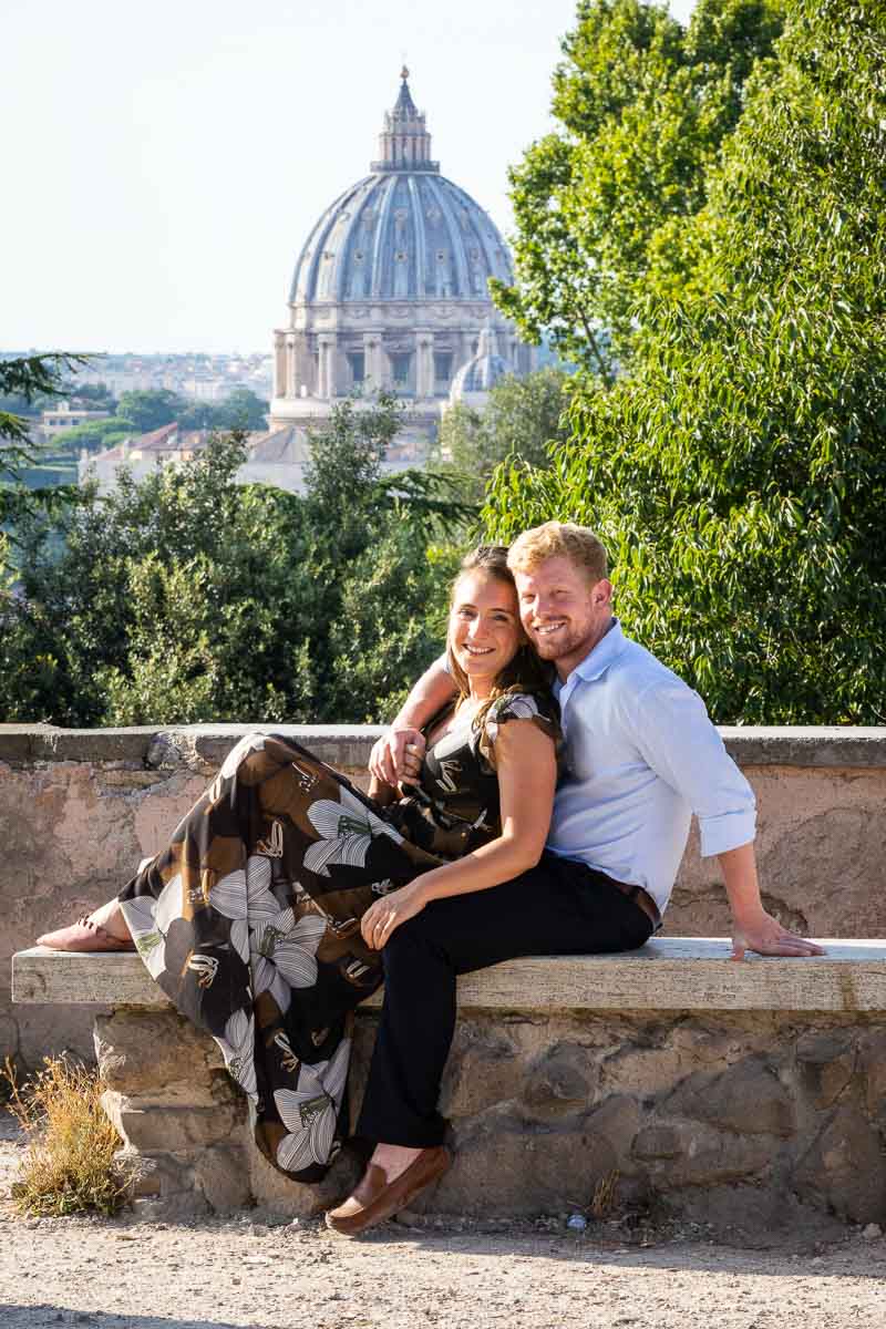 Couple portrait sitting down on a marble bench with St. Peter's Cathedral dome in the background