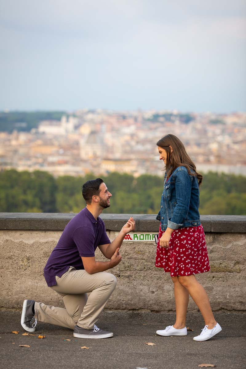 Kneed own wedding marriage proposal taking place on the Janiculum hill overlooking the city of Rome from a nearby hill