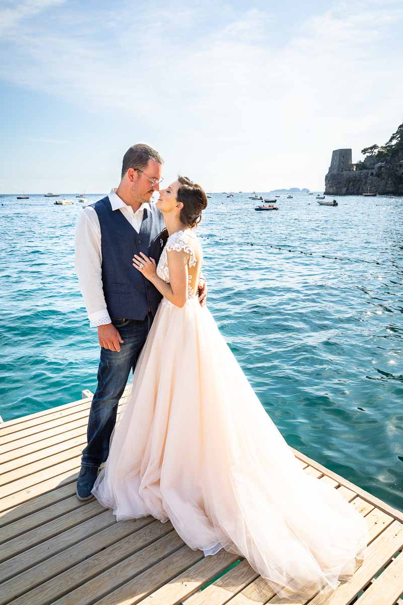Couple just married taking pictures on a wooden jetty in the middle of the sea with the horizon in the background. Elopement Wedding in Positano