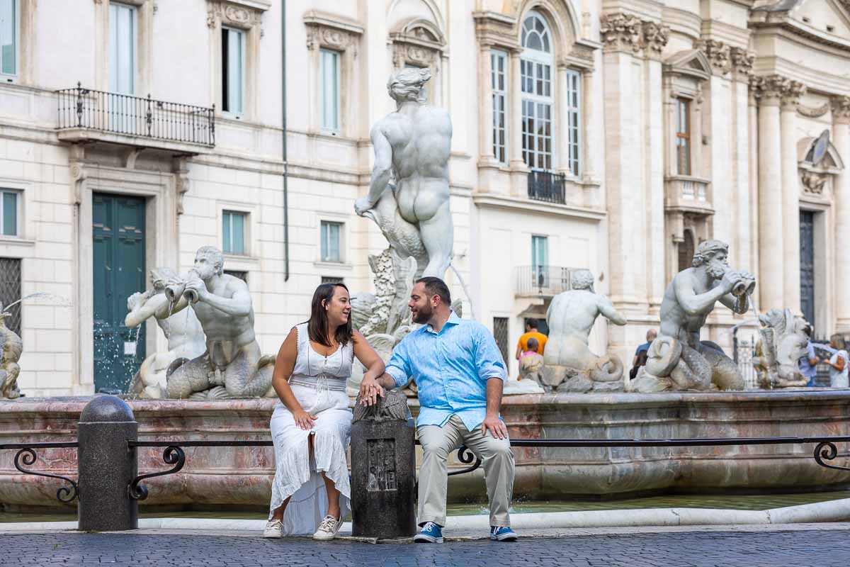 Looking at each other while sitting down on the edge of a water fountain found in the edge of the piazza navona square