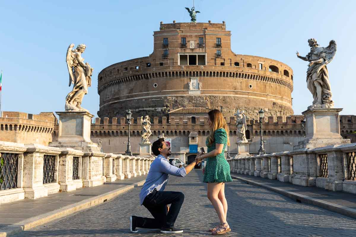 Man knee down wedding marriage proposal photography on Rome's Angel Castle bridge in the early morning. Castel Sant'angelo Bridge Proposal photography 