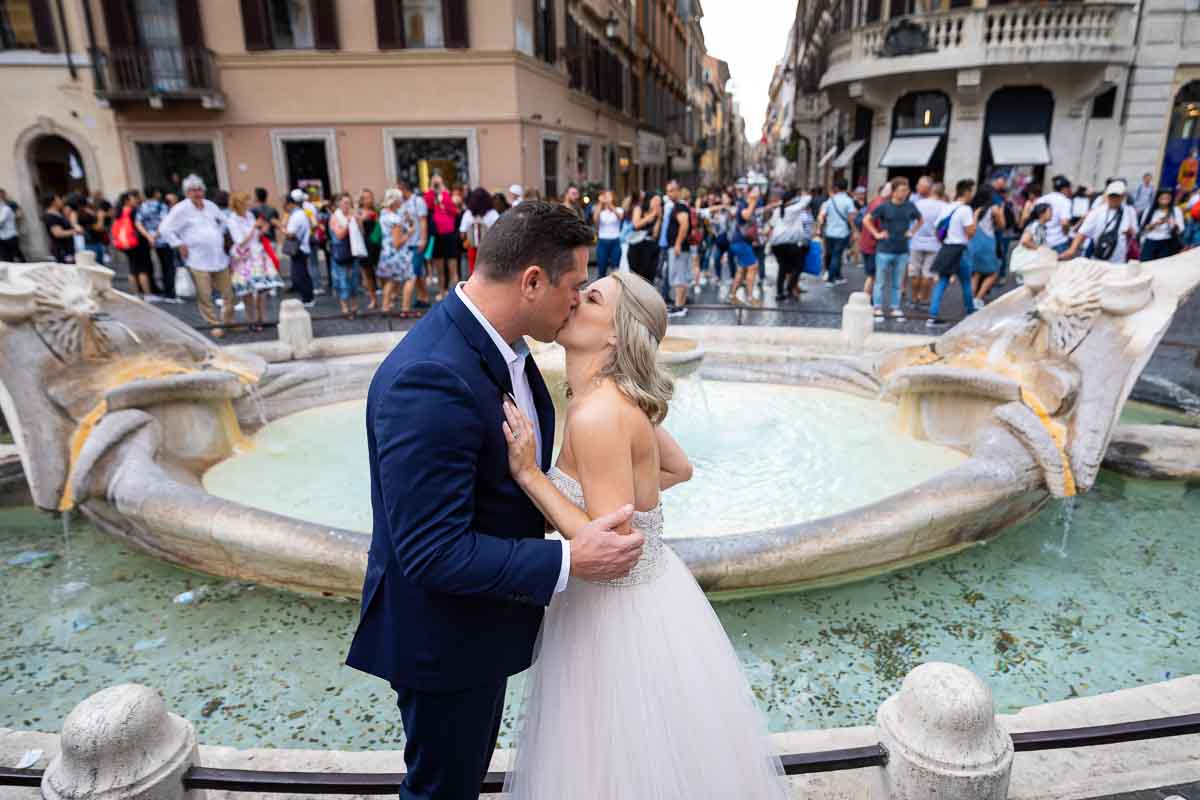 Bride and groom kissing before the barcaccia water fountain found at the bottom of Roma Piazza di Spagna