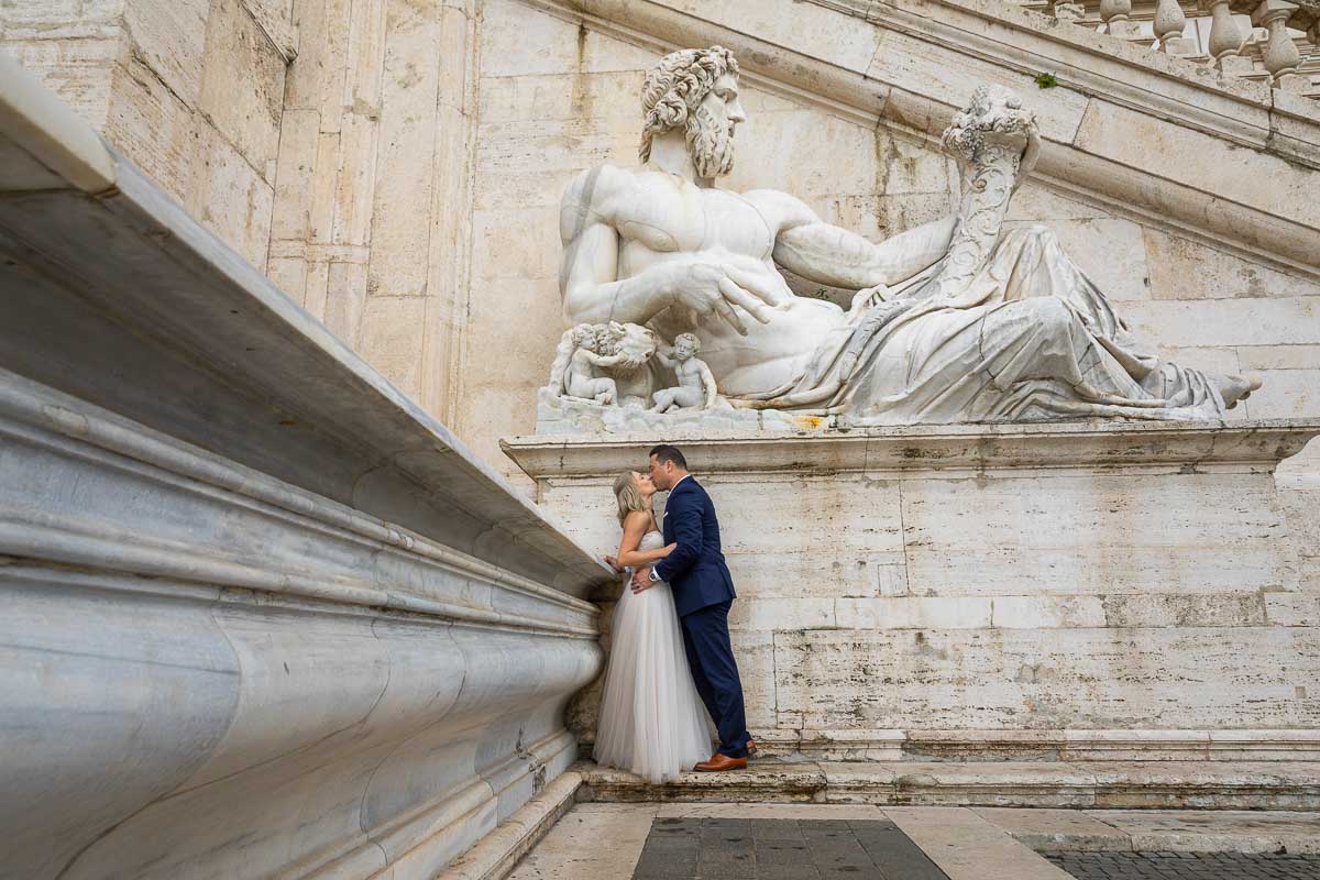 Kissing underneath a large white marble roman statue at Piazza del Campidoglio