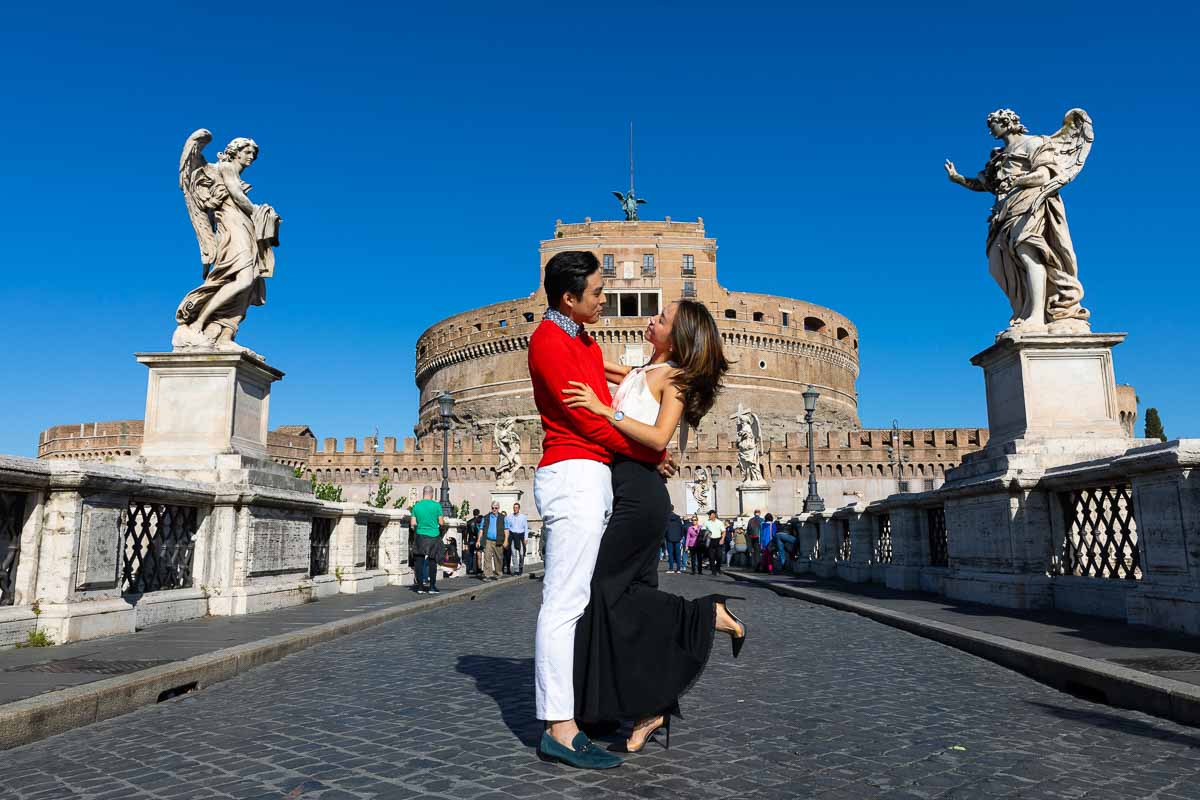 Couple posing for a picture taken on top of the Castello Sant'Angelo ponte bridge with the angel statues on either side