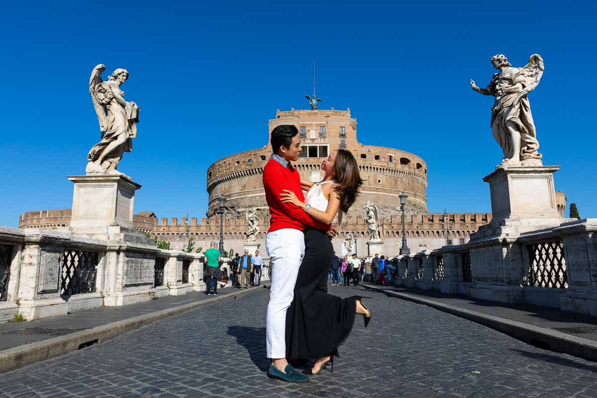 Couple posing for a picture taken on top of the Castello Sant'Angelo ponte bridge with the angel statues on either side
