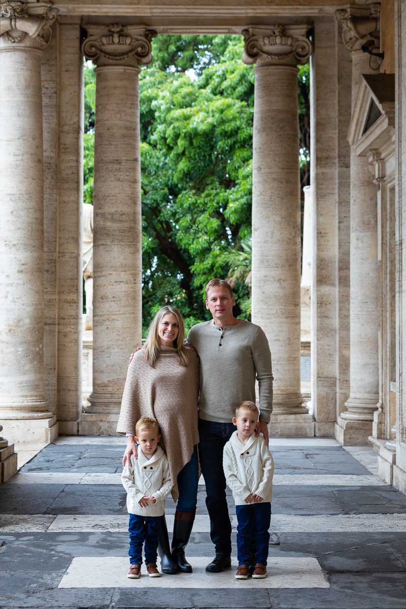 Family taking photos underneath column porticos with green tree in the backdrop 