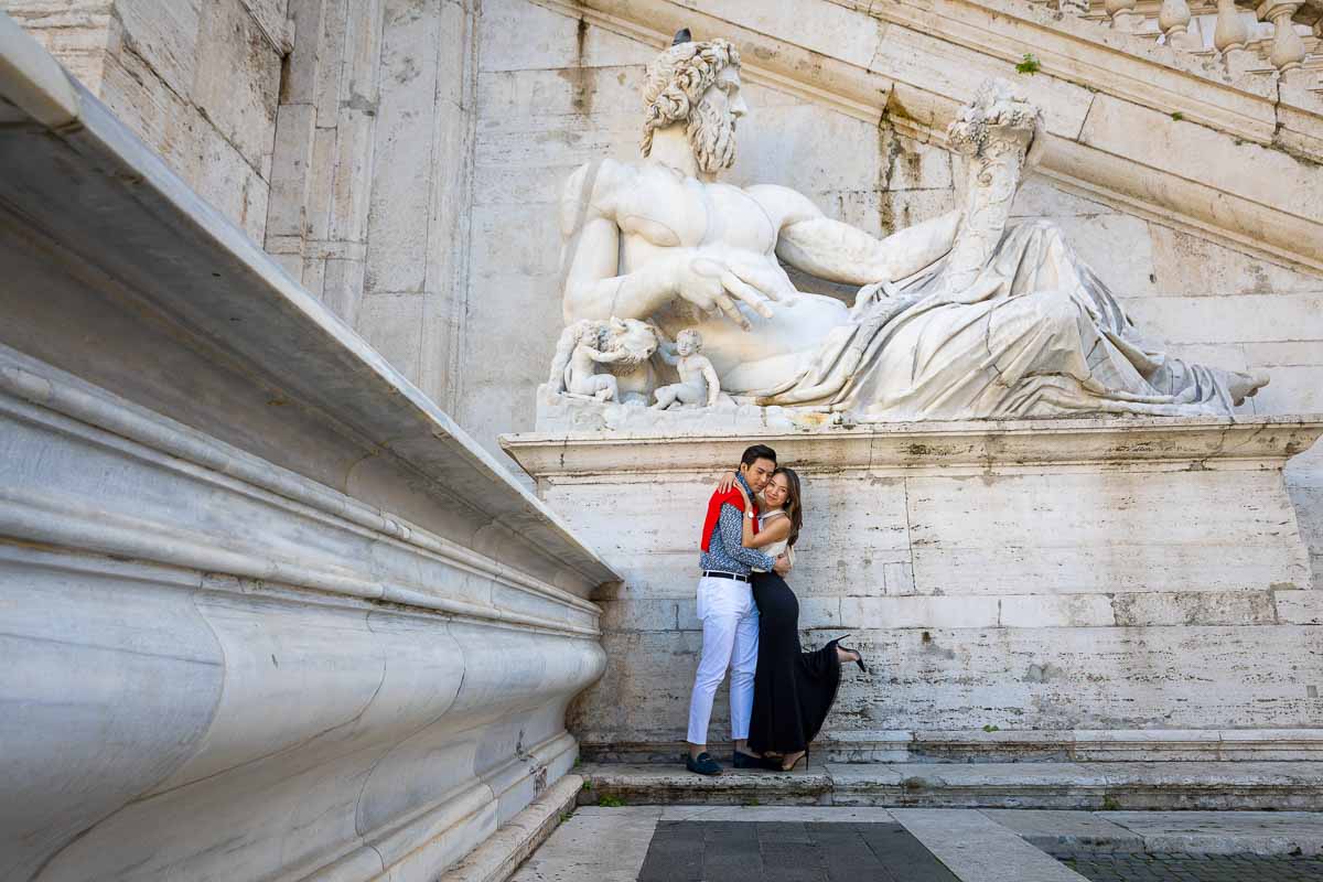 Couple portrait image taken underneath ancient white marble roman statue 