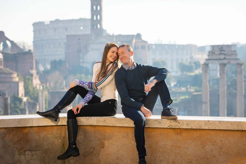 Couple sitting down on a ledge before the distant view of the roman coliseum in Rome Italy during a photoshoot