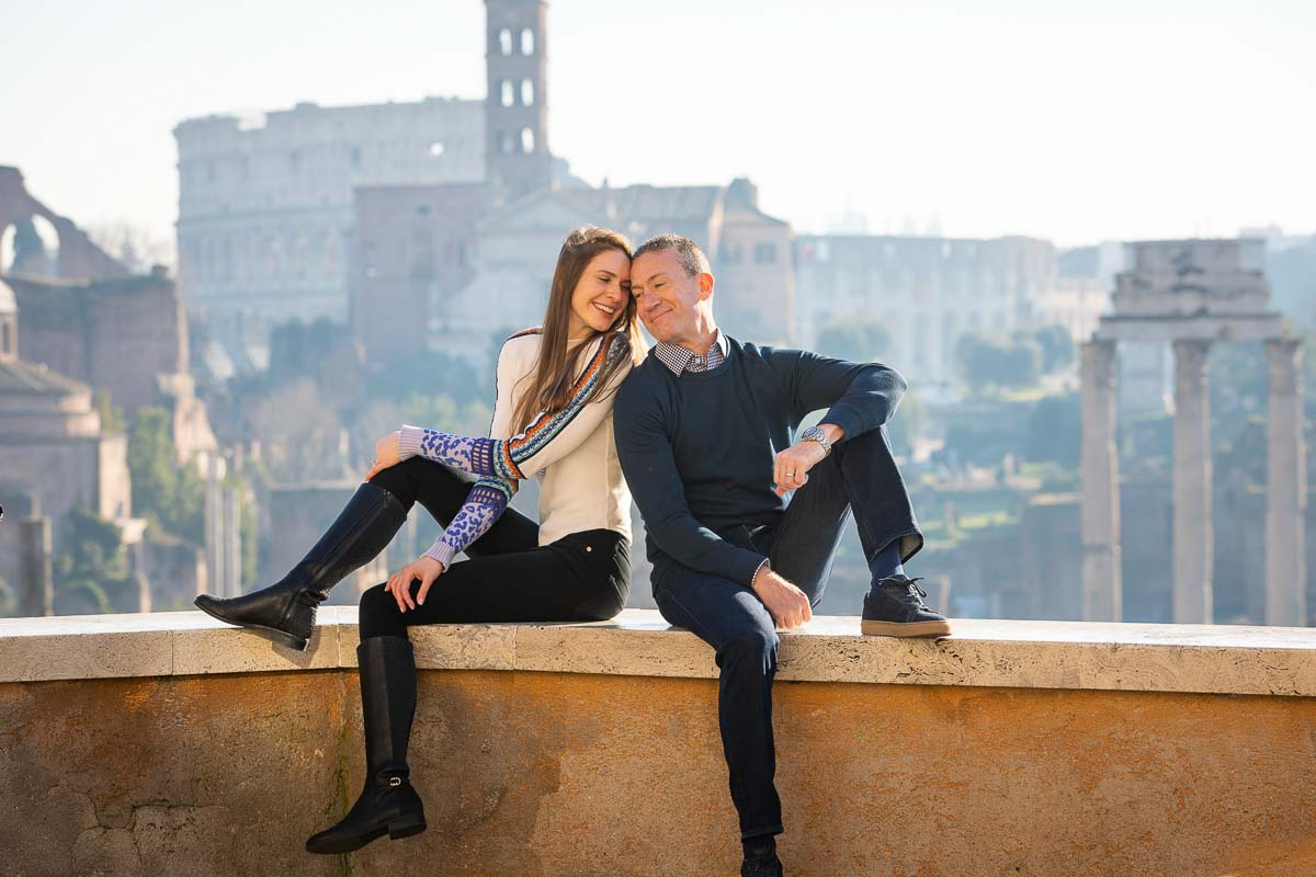 Couple sitting down on a ledge before the distant view of the roman coliseum in Rome Italy during a photoshoot