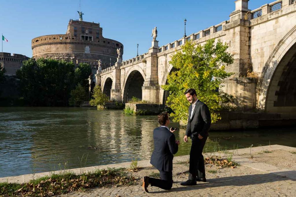 Knee down gay wedding proposal candidly photographed on the Tiber river bank with the unique view of the Castel Sant'Angelo castle in the background