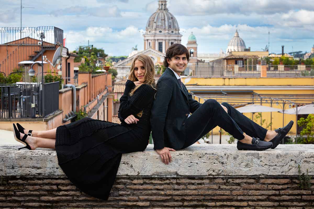 Sitting down image of a couple during an engagement session photographed in front of the panoramic view of the roman skyline