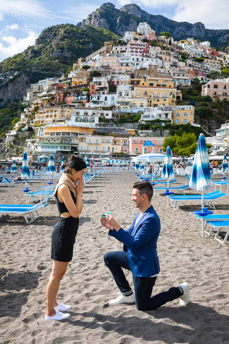 One knee down wedding marriage proposal on the beach overlooking the town of Positano in the far distance