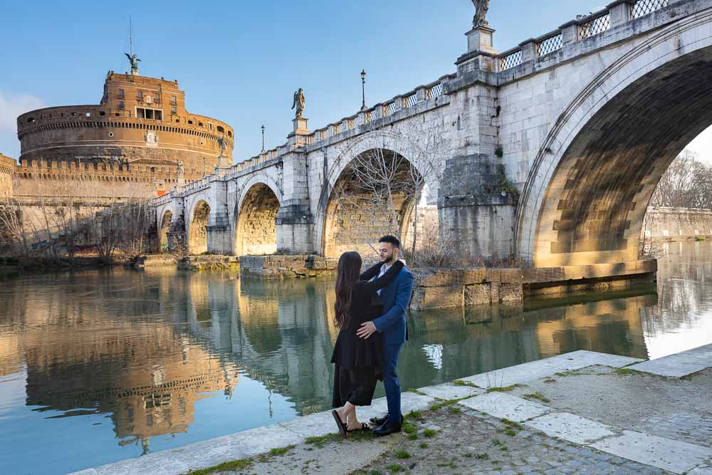 Engagement photo session down below the Tiber river bank with the castle and bridge in the far distance