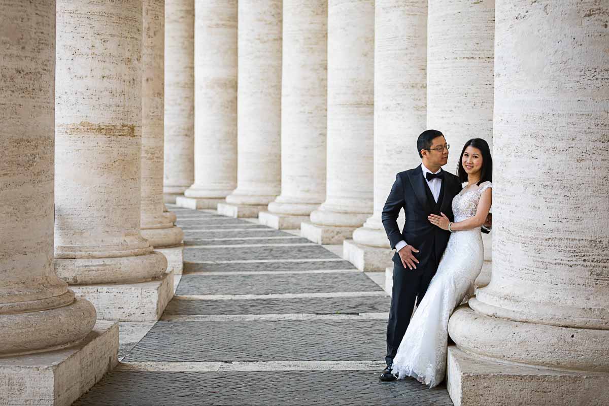 Couple posing underneath the Vatican's colonnade dressed in wedding attire