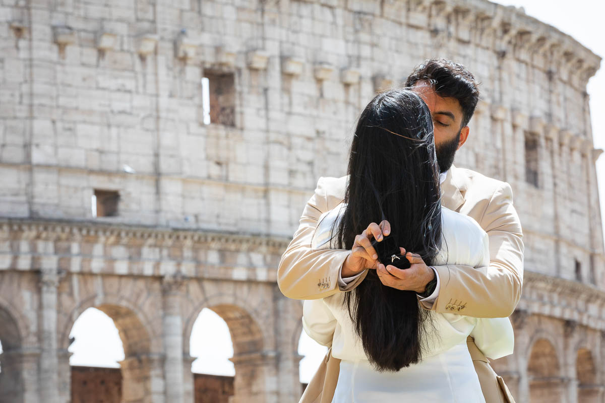 Man holding engagement ring behind his fiancée's back and showing it to the camera. Proposal Photoshoot in Rome Italy.