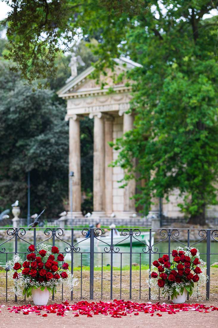 A small angle in the Villa Borghese lake set up by the lake for a romantic wedding marriage proposal using 2 vases of red roses together with rose petals on the ground