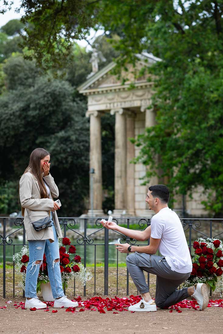 Romantic Rome Proposal. Knee down Surprise Wedding Proposal at the Villa Borghese lake among beautiful red roses 