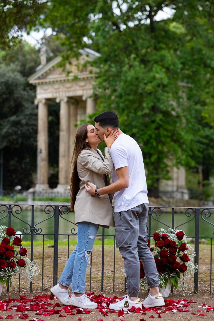Engaged in Rome by the Borghese park among a bouquet of red roses and a scenic view over the lake and the temple