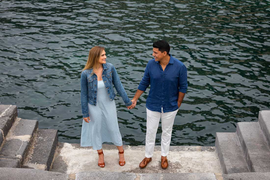 Holding hands while looking at each other with the Mediterranean sea as backdrop