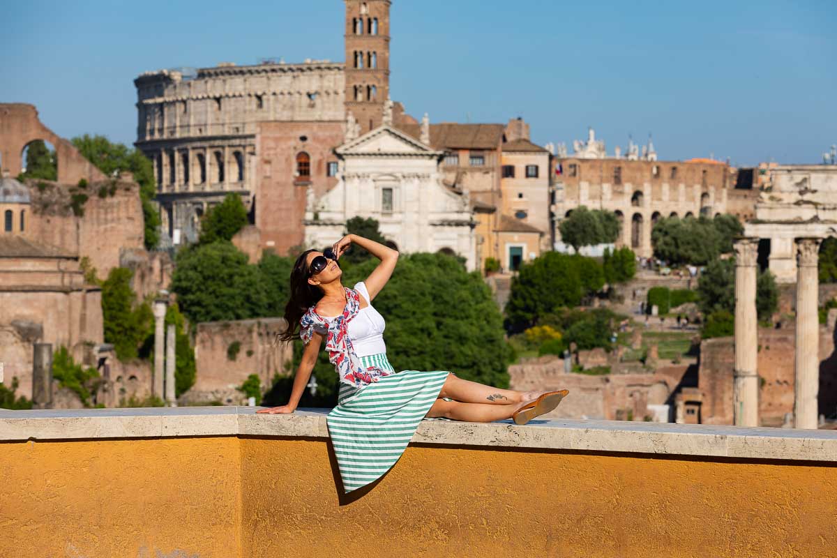 Sitting down portrait picture on a bright orange wall with the Roman Colosseum in the far distance