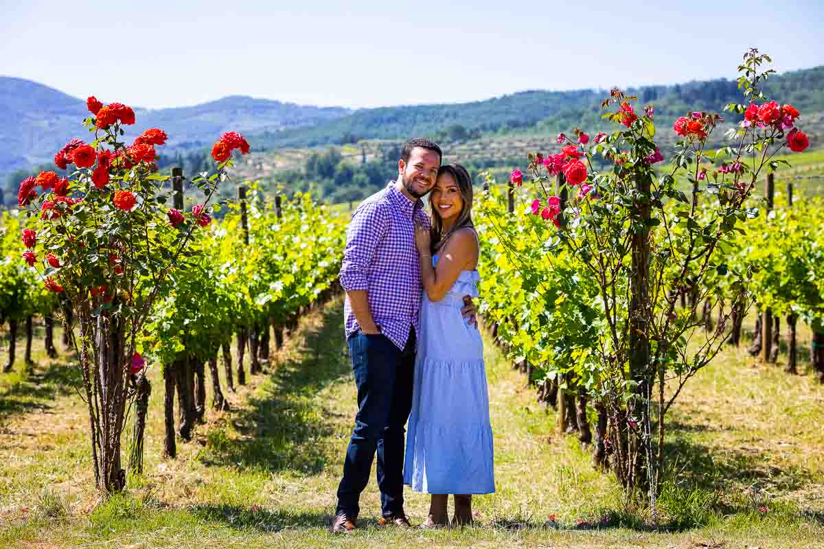 Portrait of a couple together posing in front of the row vineyard where beautiful red roses were placed. Posing after a Tuscany Vineyard Wedding Proposal