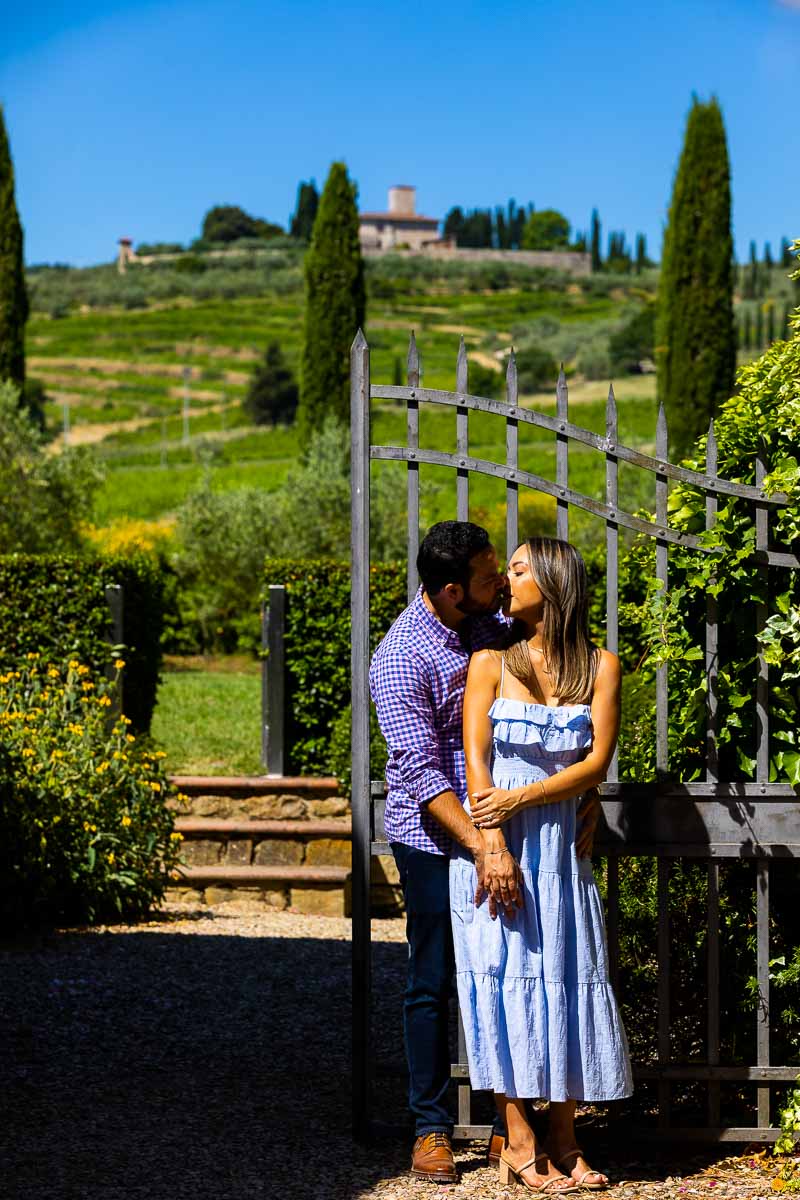 Posed image of a couple together photographed in front of a gate and Tuscan towns in the backdrop. Vineyard Wedding Proposal in Tuscany
