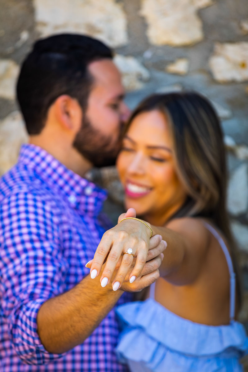 Engagement ring close up in focus with the couple out of focus in the background. Wedding Proposal in Tuscany in a vineyard. Engagement photos