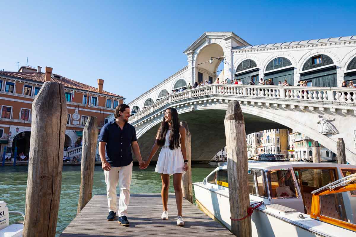 Walking together on a jetty in front of Ponte Rialto and next to docked boats