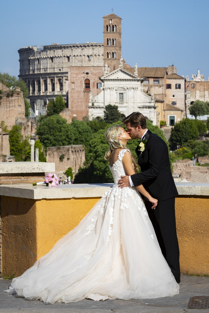 Newlyweds kissing with the view of the roman colosseum in the far distance