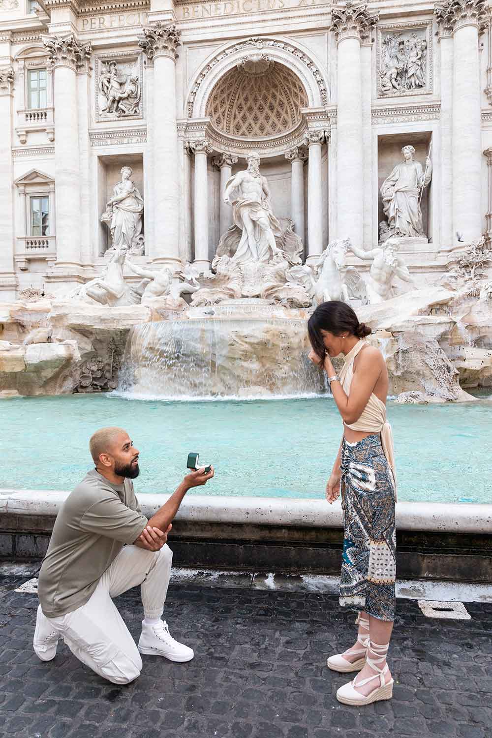 Knee down surprise wedding proposal photographed at the Trevi fountain in the early morning to avoid crowds. Turning out to be a really romantic Trevi proposal