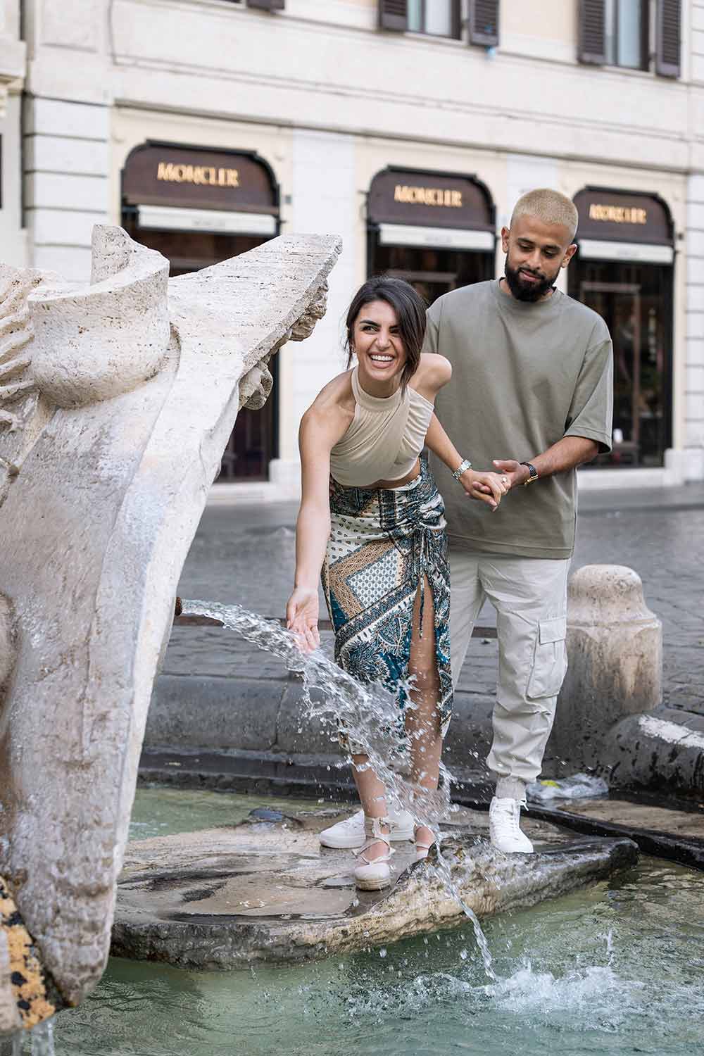 Portrait picture of a couple getting some water from the Barcaccia water fountain, found at the bottom of the Spanish steps in Rome Italy