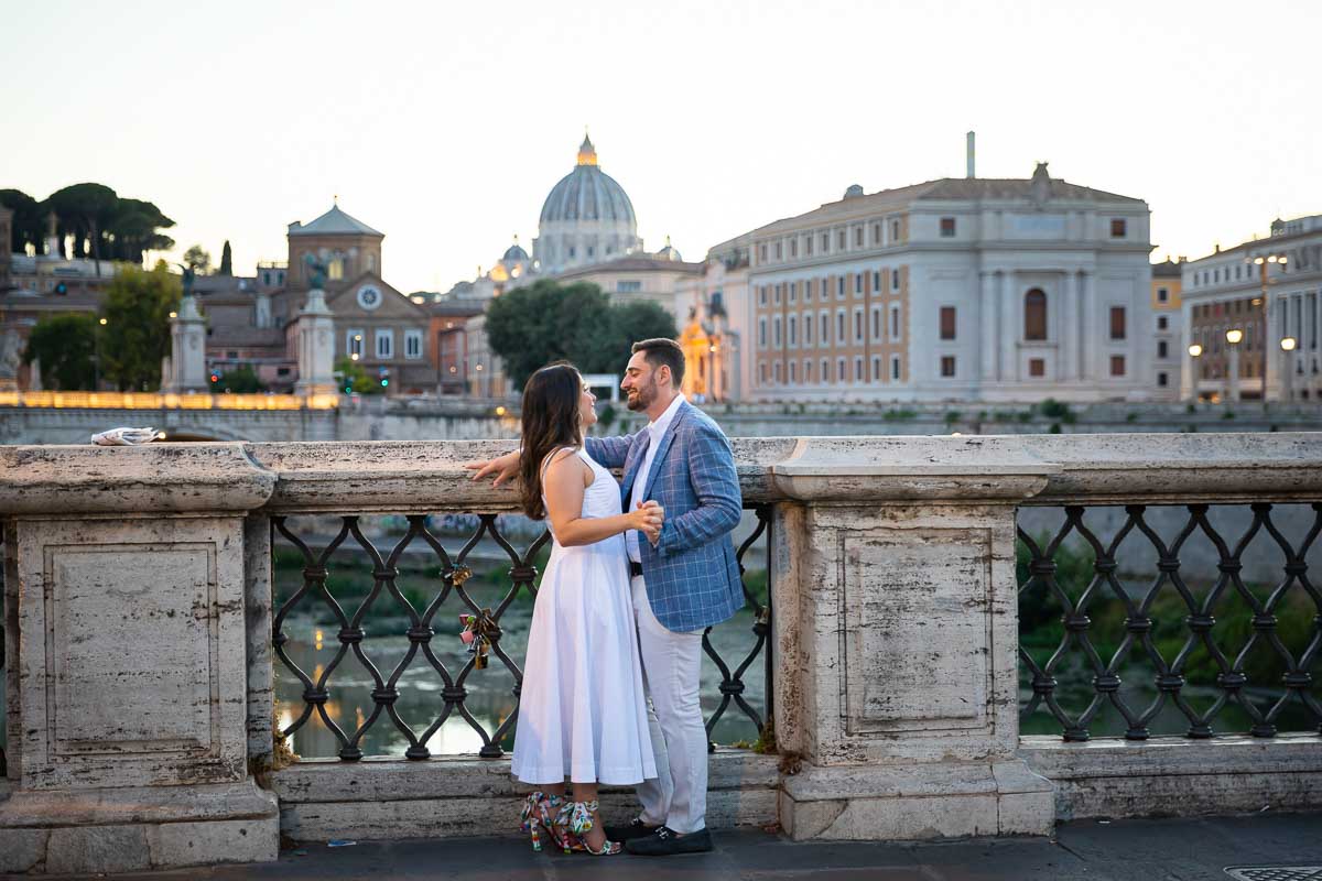 Final portrait picture of a couple standing on the Castel Saint Angel bridge with the last rays of light shining on the distant dome of Saint Peter in the Vatican 