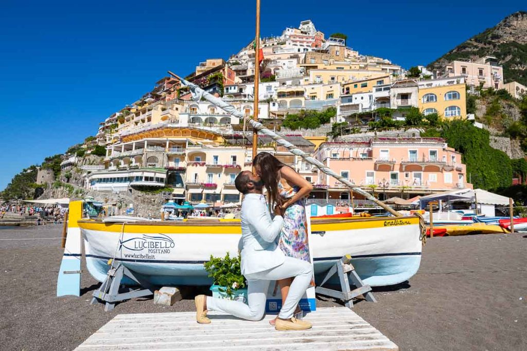Kissing in Positano during a couple photoshoot in front of a fishermen's boat and the vertical town in the backdrop