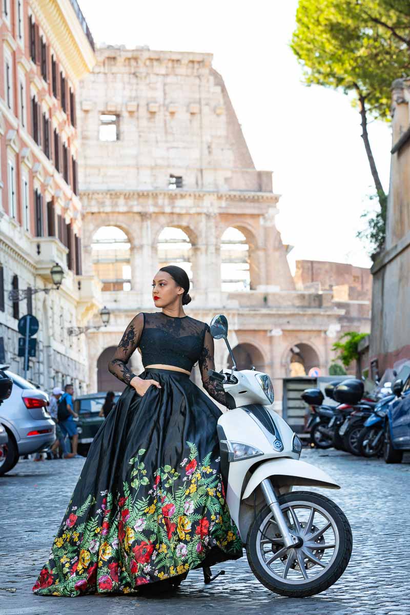 Model picture sitting on a white scooter before the massive view of the Roman Colosseum photographed during a photoshoot in Rome